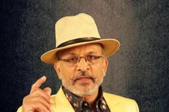 Annu Kapoor smiling portrait in a black suit, showcasing his journey from Bollywood actor to TV host and singer