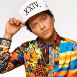 Bruno Mars smiling on stage with a microphone, celebrating his birthday and musical achievements in a vibrant concert setting.