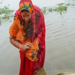 Chhath Puja Sandhya Arghya 2024 में महिलाएं सूर्य देवता को जल अर्पित करते हुए, जिसमें पूजा का अर्थ, विधि और लाभ दिखाया गया है | Women offering water to Sun God during Chhath Puja evening ritual, showcasing meaning, steps, and benefits in Hindi and English