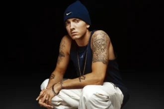 Eminem posing seriously in a black hoodie, with text overlay in Hindi and English highlighting his rise from Detroit struggles to global hip-hop fame, symbolizing his inspirational journey.
