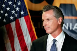 Gavin Newsom portrait with Hindi text 'गेविन न्यूसम की प्रेरणादायक जीवन यात्रा' on AajKyaHai.com