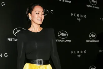 Gong Li smiling in a red dress, with Hindi text overlay 'गोंग ली की प्रेरणादायक कहानी' and English text 'Gong Li's Inspiring Journey'