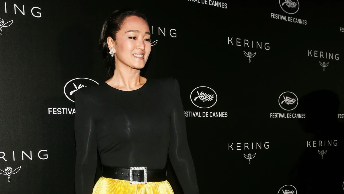 Gong Li smiling in a red dress, with Hindi text overlay 'गोंग ली की प्रेरणादायक कहानी' and English text 'Gong Li's Inspiring Journey'