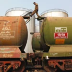 Indian Prime Minister Narendra Modi and Russian President Vladimir Putin shaking hands at an energy summit, with Indian and Russian flags in the background, symbolizing continued oil trade partnership despite US pressure