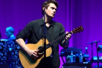 John Mayer playing guitar on stage, showcasing his musical talent as a guitar virtuoso and songwriting genius
