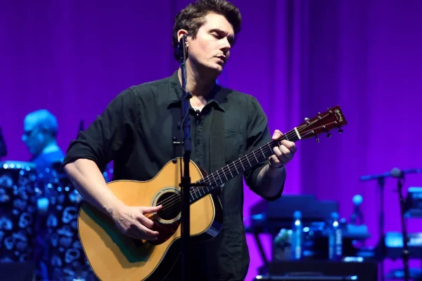 John Mayer playing guitar on stage, showcasing his musical talent as a guitar virtuoso and songwriting genius