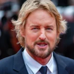 Owen Wilson smiling in a candid photo, with text overlay in Hindi and English highlighting his inspiring journey from struggles to Hollywood stardom